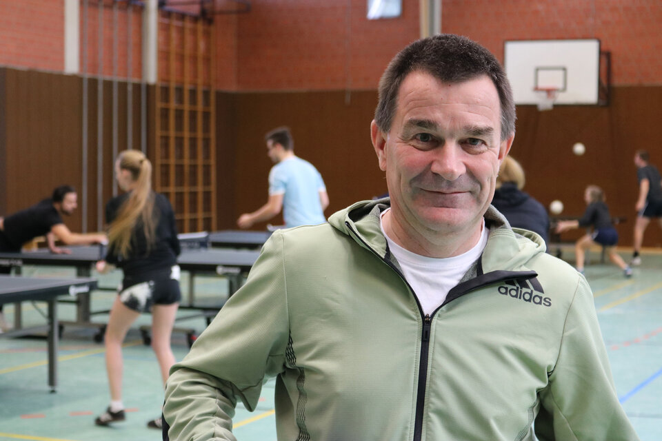Mathias Hornberger steht in einer Sporthalle. Im Hintergrund spielen Personen Tischtennis.