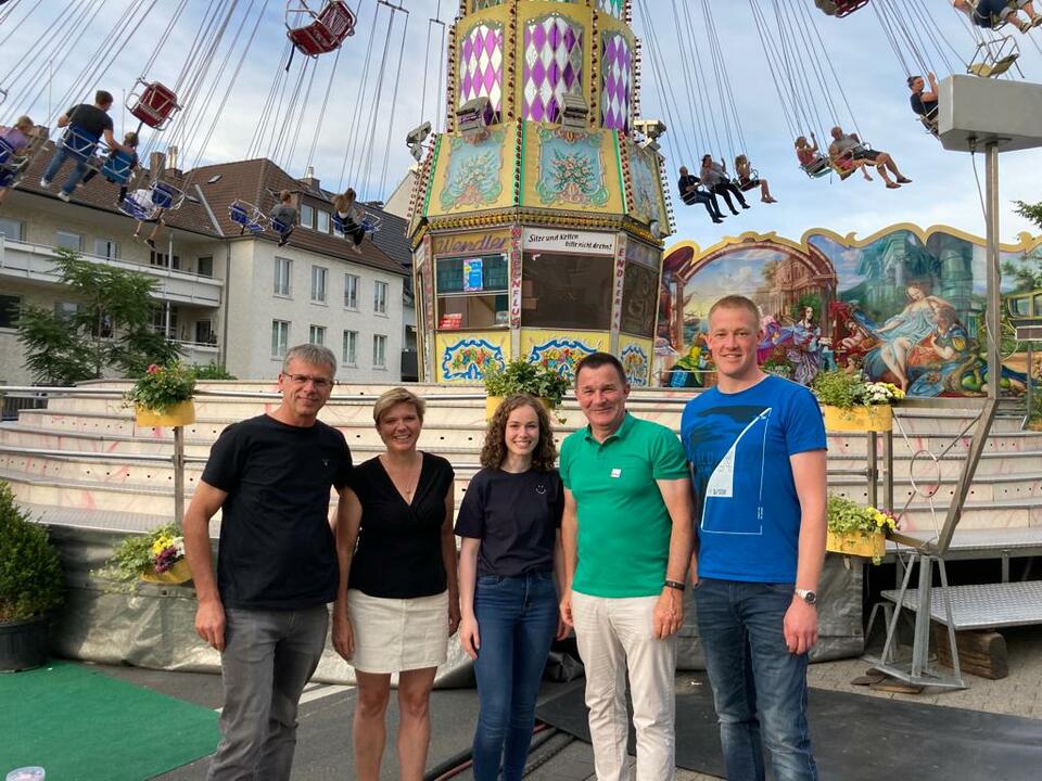 Unser geschäftsführender Vorstand und unsere Geschäftsstellenleiterin stehen vor einem Kettenkarussell und lächeln in die Kamera.